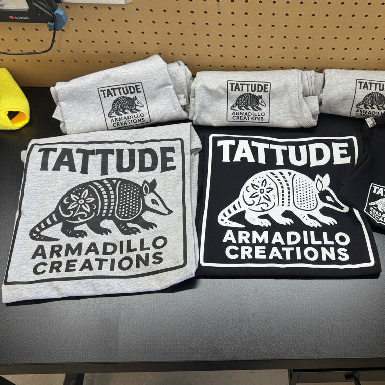 T-shirts with 'Tattitude Armadillo Creations' design on a table.